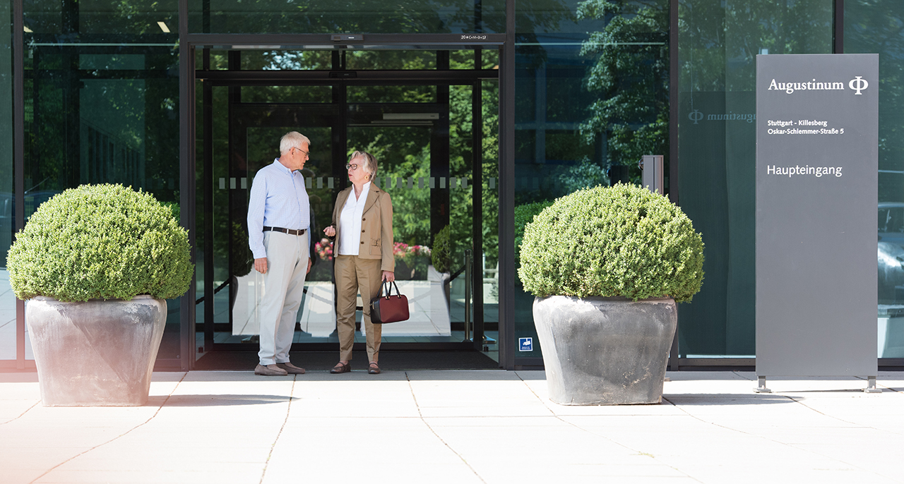 Ein Seniorenpaar steht vor dem Eingang des Augustinum