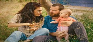 junges Paar mit Baby sitzt im Gras - Szene aus "Sorda"