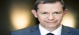 Mann in Anzug, weißem Hemd und Krawatte vor Gegenlicht