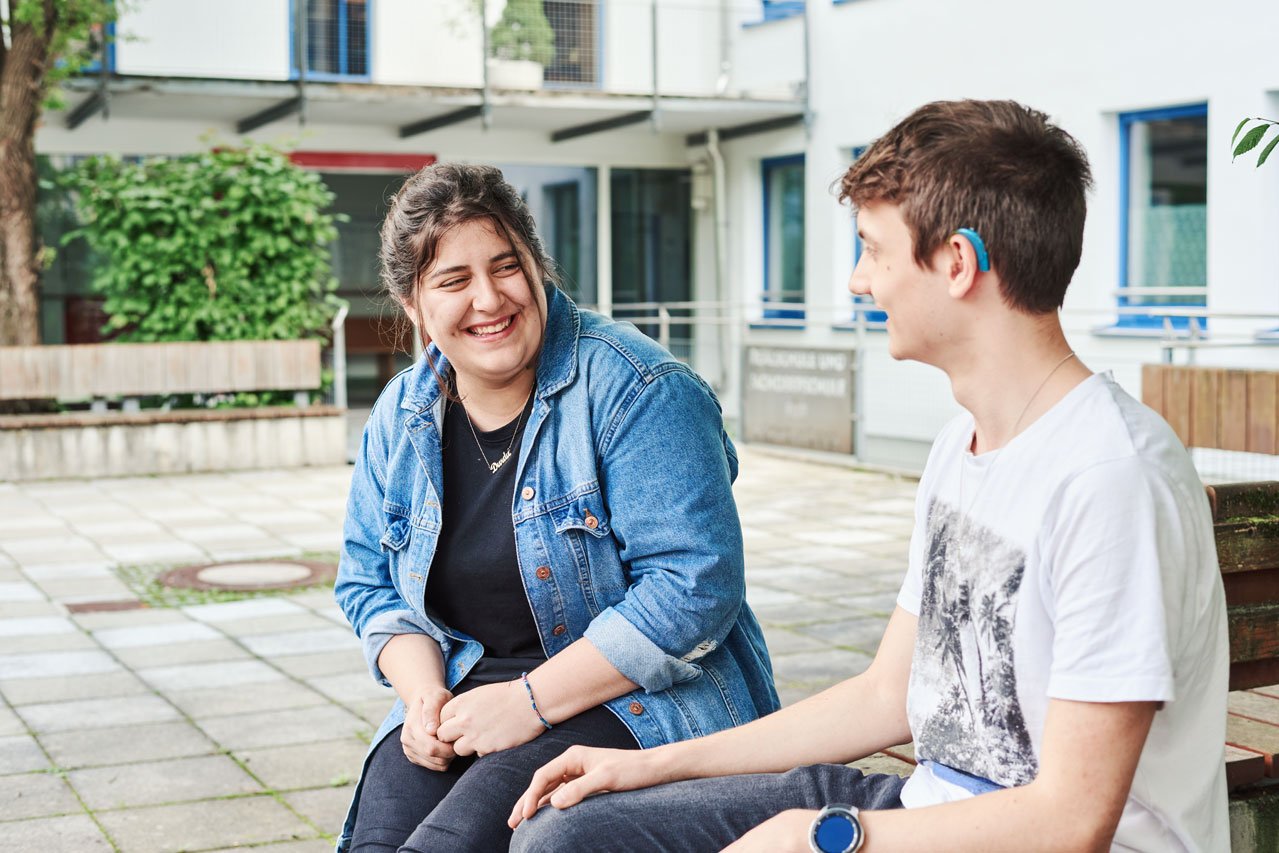 Freizeit im Pausenhof Zwei Schüler*innen sitzen auf einer Bank im Pausenhof und unterhalten sich