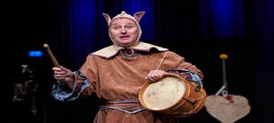 Ein als Hofnarr gekleideter Mann mit Trommel auf einer Bühne