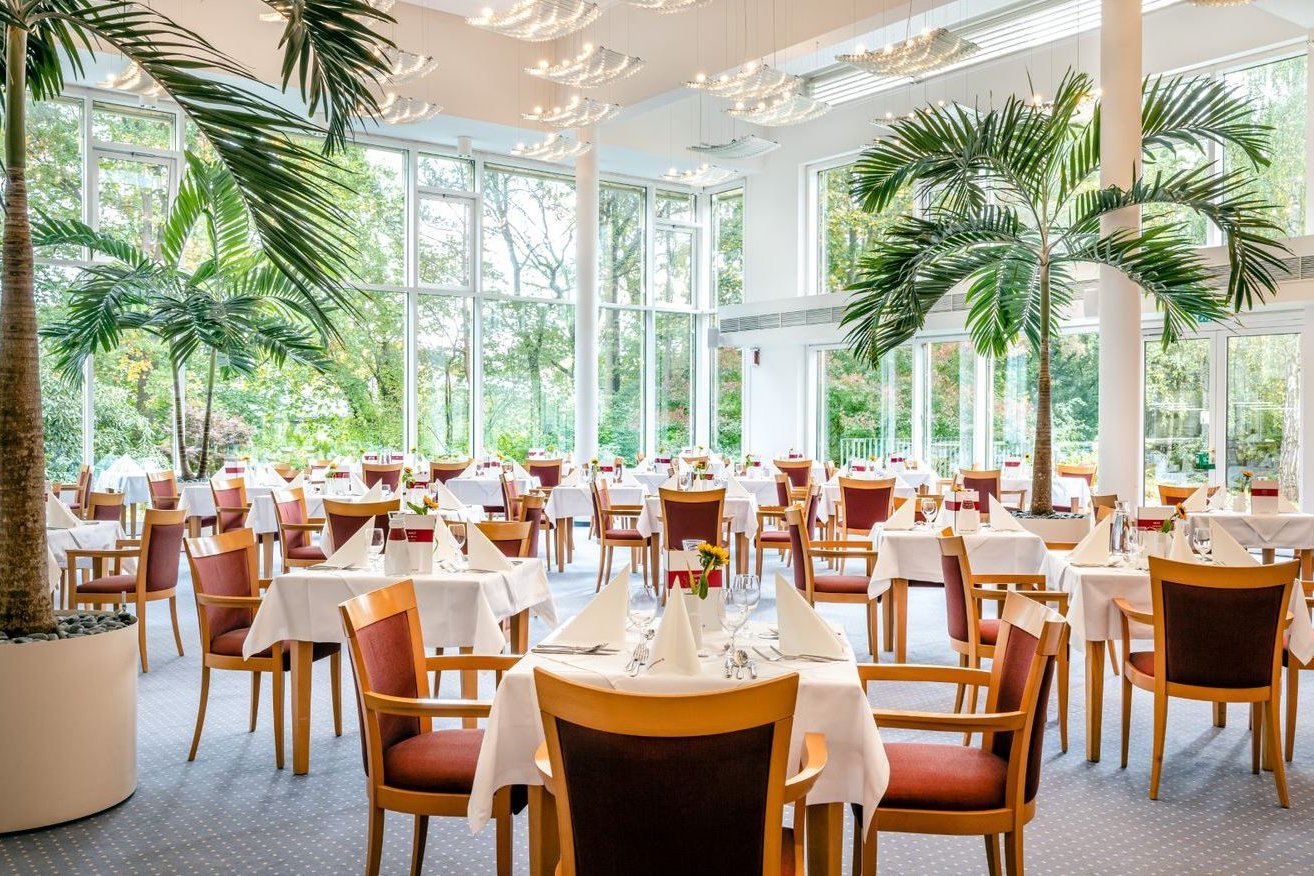 Im 2019 komplett renovierten Restaurant werden mittags verschiedene Drei-Gänge-Menüs sowie eine Auswahl an Gerichten à la carte serviert. Gedeckte Tische in einem Restaurant mit großen Fenstern