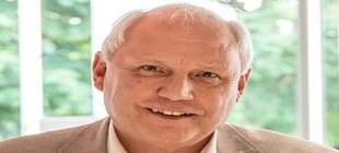 Mann in hellem Anzug vor einem grünen Hintergrund