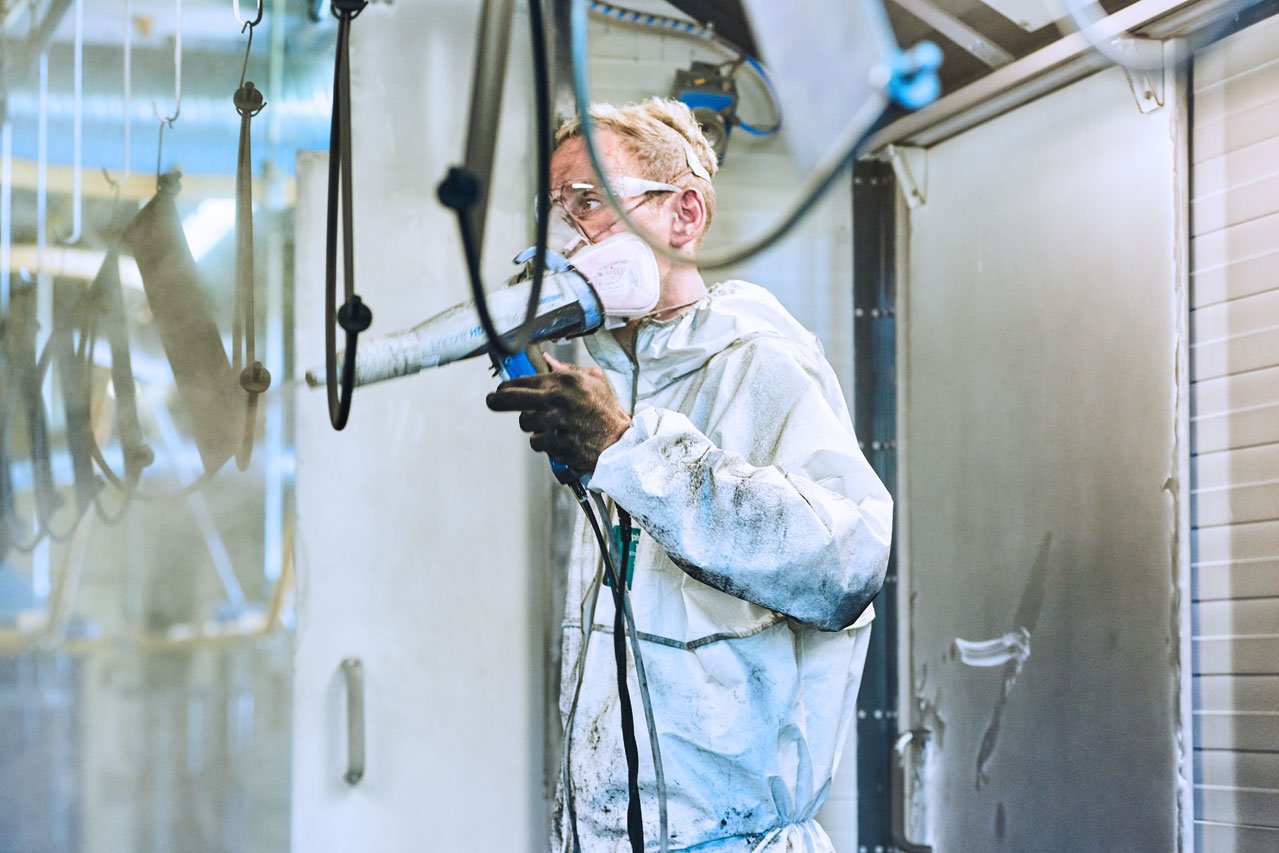 Pulverbeschichtungsraum Ein Klient im weißen Schutzanzug mit einer Pulverbeschichtungspistole in der Hand