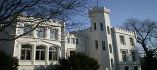 Ein weißes Gebäude mit Zinnen und Turm vor einem blauen Himmel