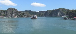 Wasserfläche mit Booten, Häusern am Ufer und mit Bergen im Hintergrund