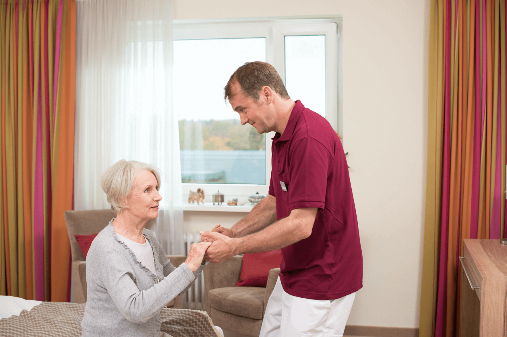 Tagesbetreuung für Menschen mit Demenz Pfleger hilft älterer Dame beim Aufstehen