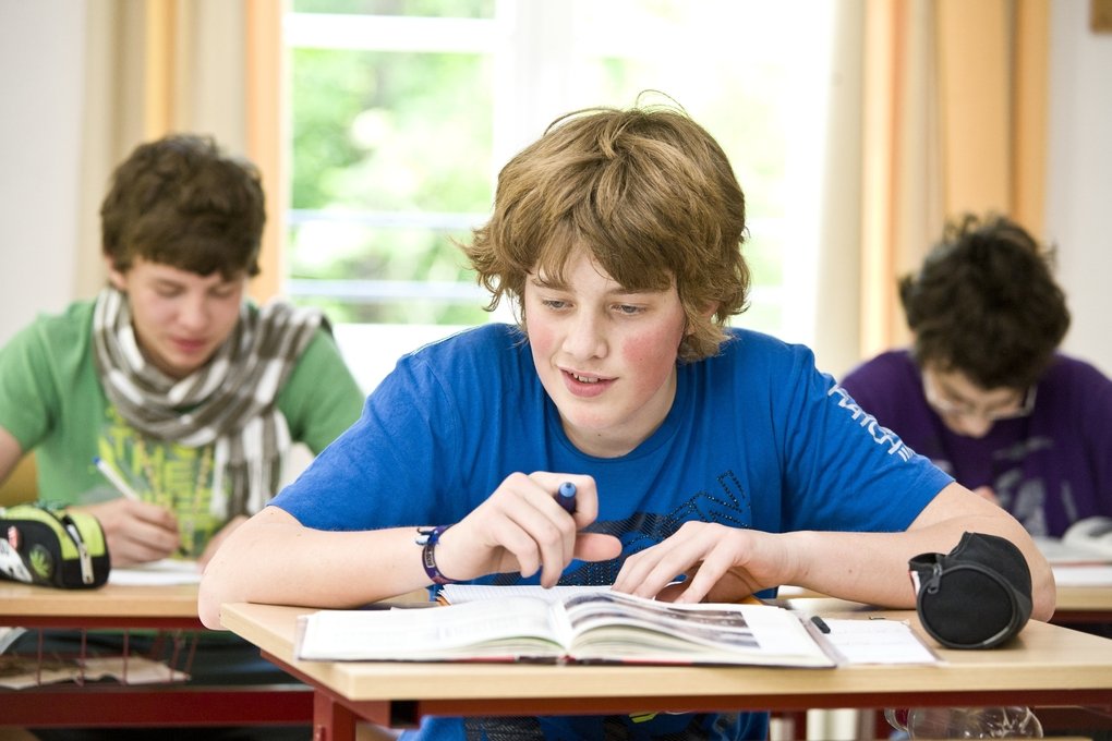 iPads zur Lernunterstützung Slider 2 Ein Junge sitzt im Unterricht und vor ihm liegen ein Heft und ein Schulbuch