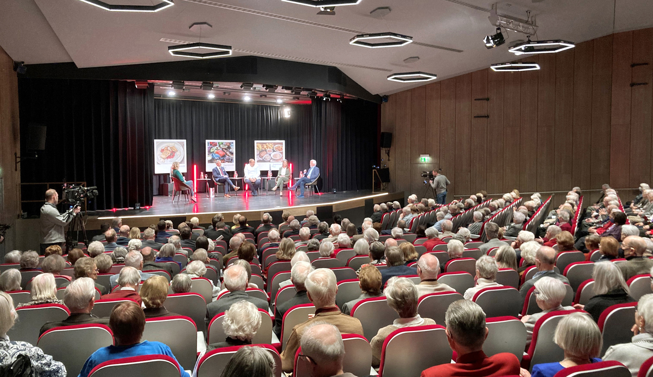 Theatersaal im Augustinum Stuttgart-Sillenbuch Senior*innen sitzen im Theatersaal während sich fünf Leute auf der Bühne unterhalten