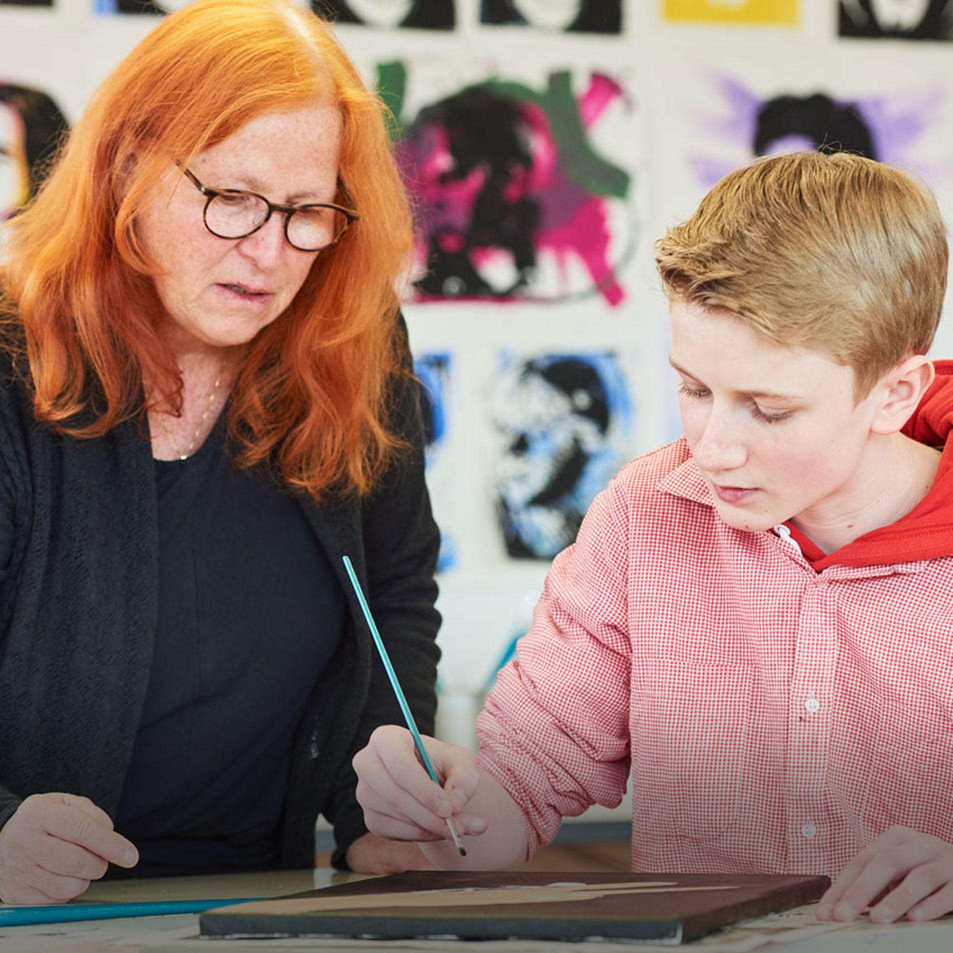Kunst Eine Lehrerin schaut einem Schüler beim Malen im Kunstunterricht zu