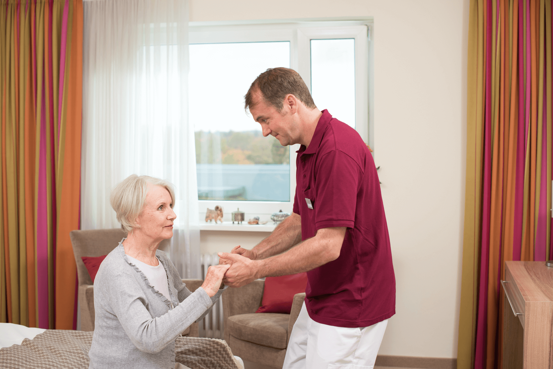 Tagesbetreuung für Menschen mit Demenz Pfleger hilft älterer Dame beim Aufstehen