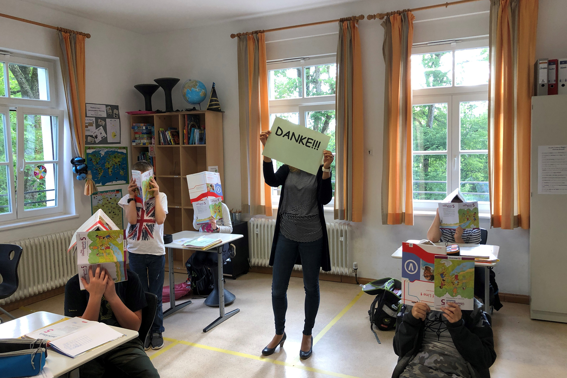 Augustinum Spenden Erfolge Slider 6 Schüler*innen im Klassenzimmer halten Schulhefte vor ihr Gesicht und die Lehrkraft bedankt sich für eine Spende für Arbeitshefte in Corona Zeiten