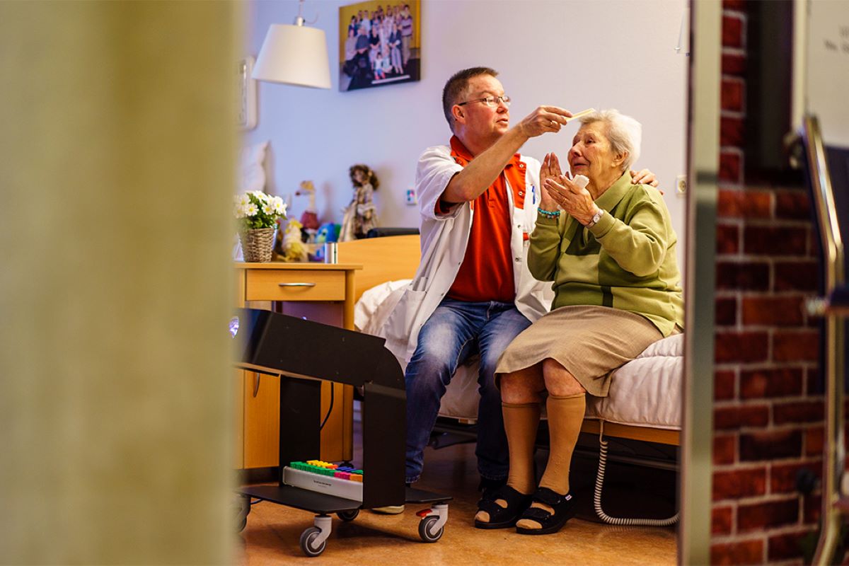 Pfleger kämmt Seniorin die Haare, auf Bett sitzend