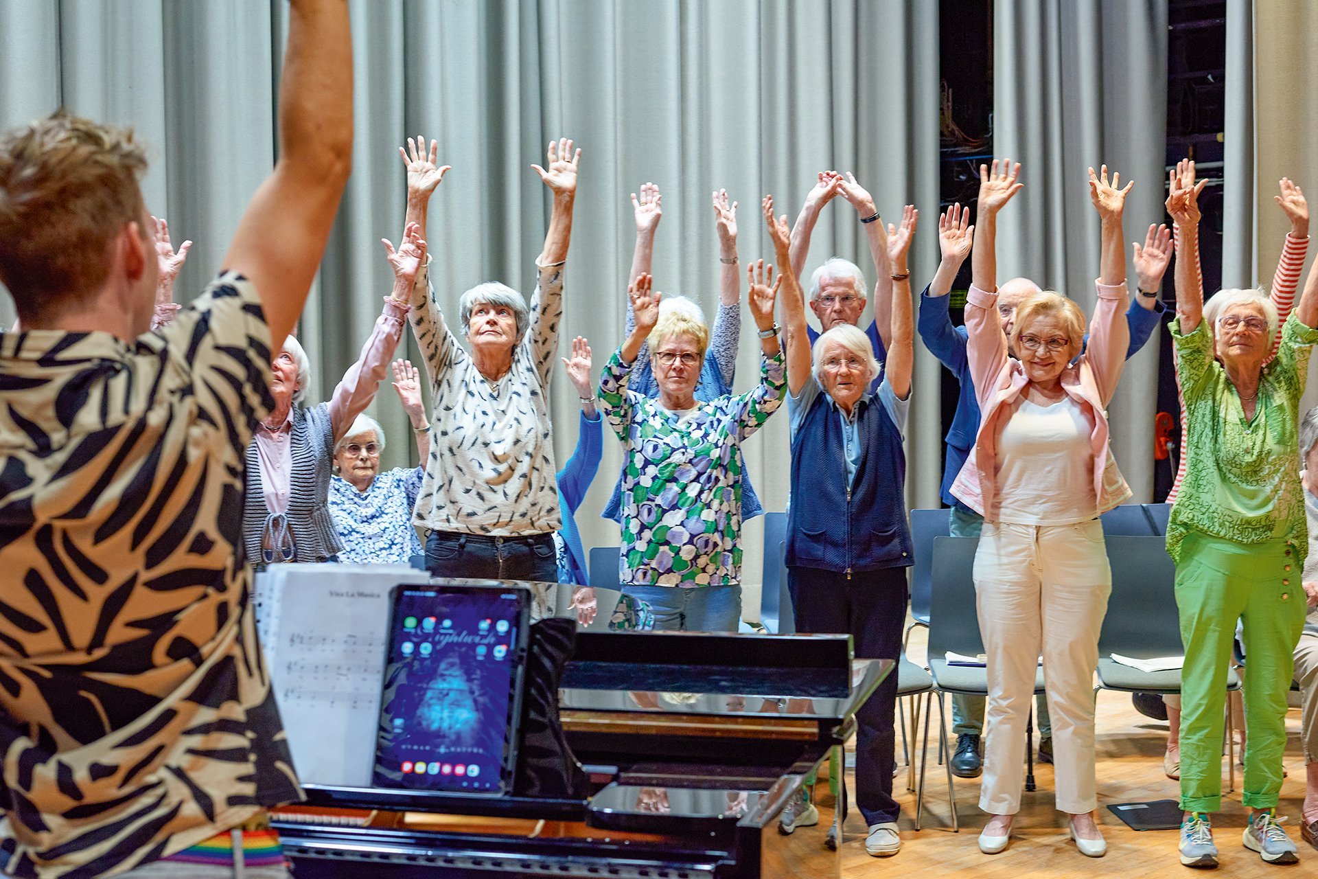 Augustinum Seniorenresidenz Bonn Theater Chor Senior*innen stehen auf der Bühne des Theatersaals und machen gemeinsam mit dem Chorleiter Gesangsübungen