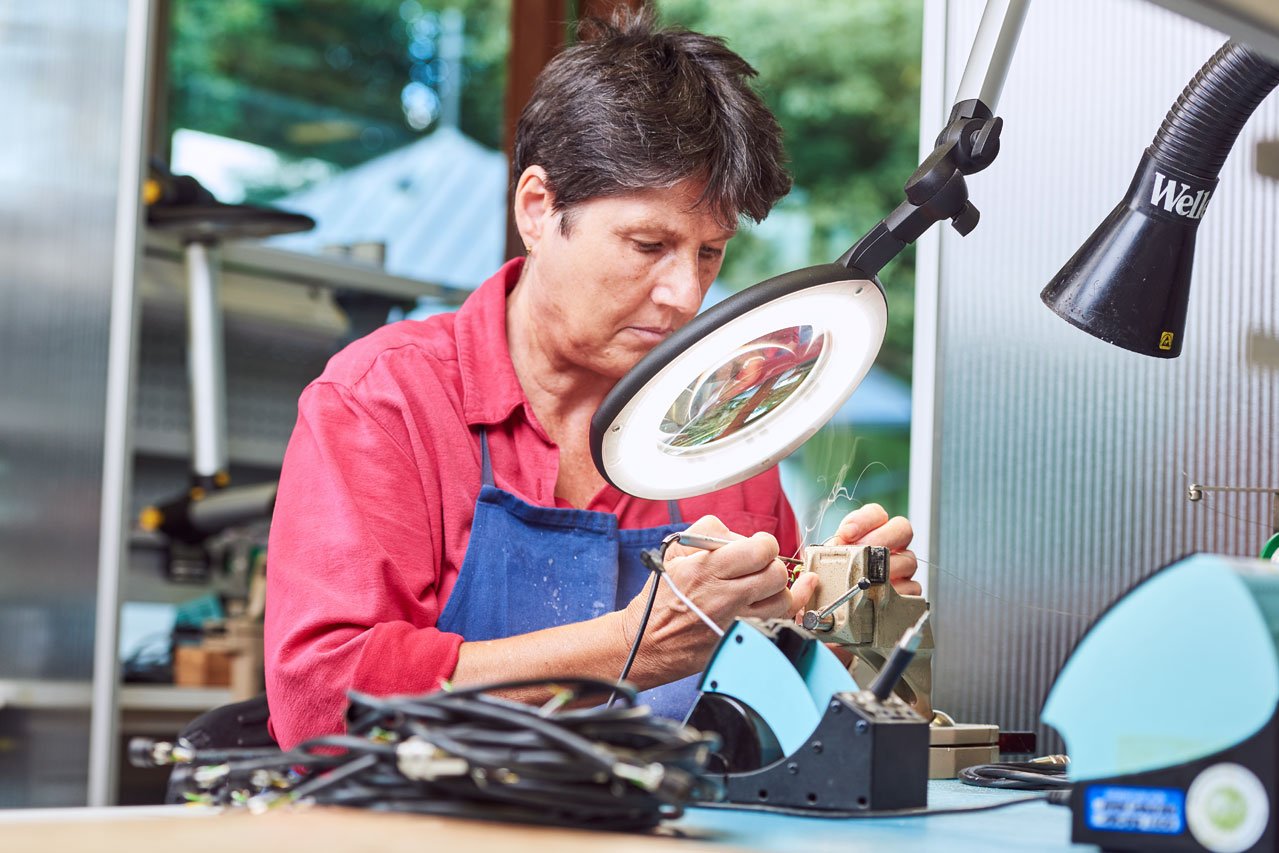 Werkstätten Elektronikabteilung Eine Klientin arbeitet mit einem Vergrößerungsglas in der Elektronikabteilung
