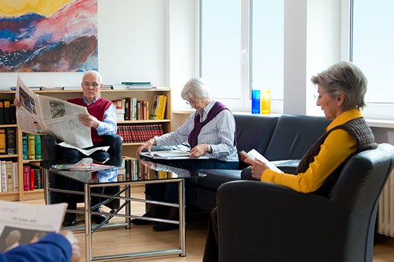 Augustinum Seniorenresidenzen Gemeinschaftsräume Vier Senior*innen lesen Zeitung in einem Gemeinschaftsraum