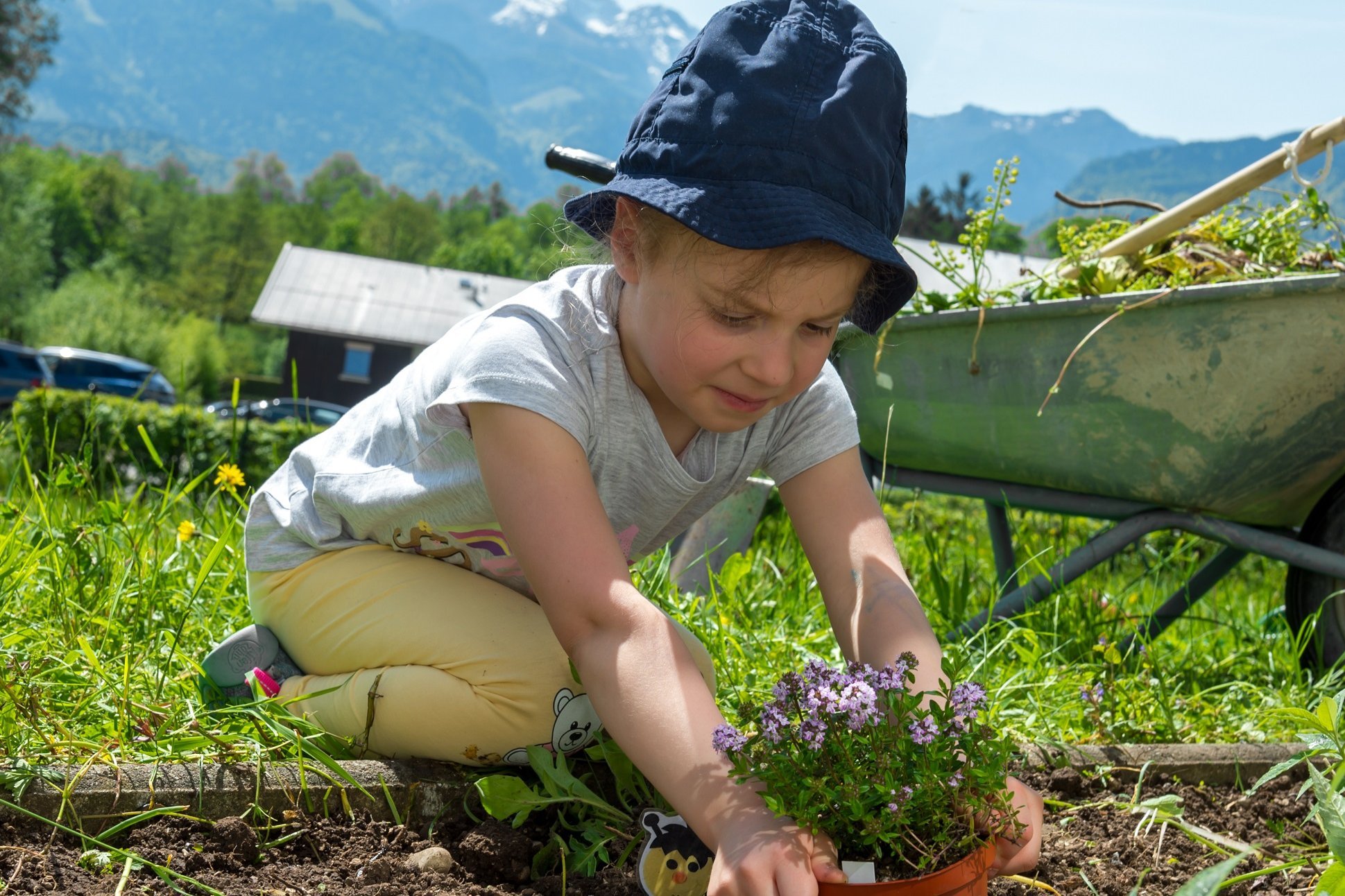 Fördern im Freien  Ein Kind sitzt in einem Garten und pflanzt eine Pflanze ein