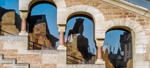 Mittelalterliche Fensteröffnungen mit Rundbögen und Säulen; Burgplatz Braunschweig, Braunschweiger Burglöwe spiegelt sich im Fensterglas