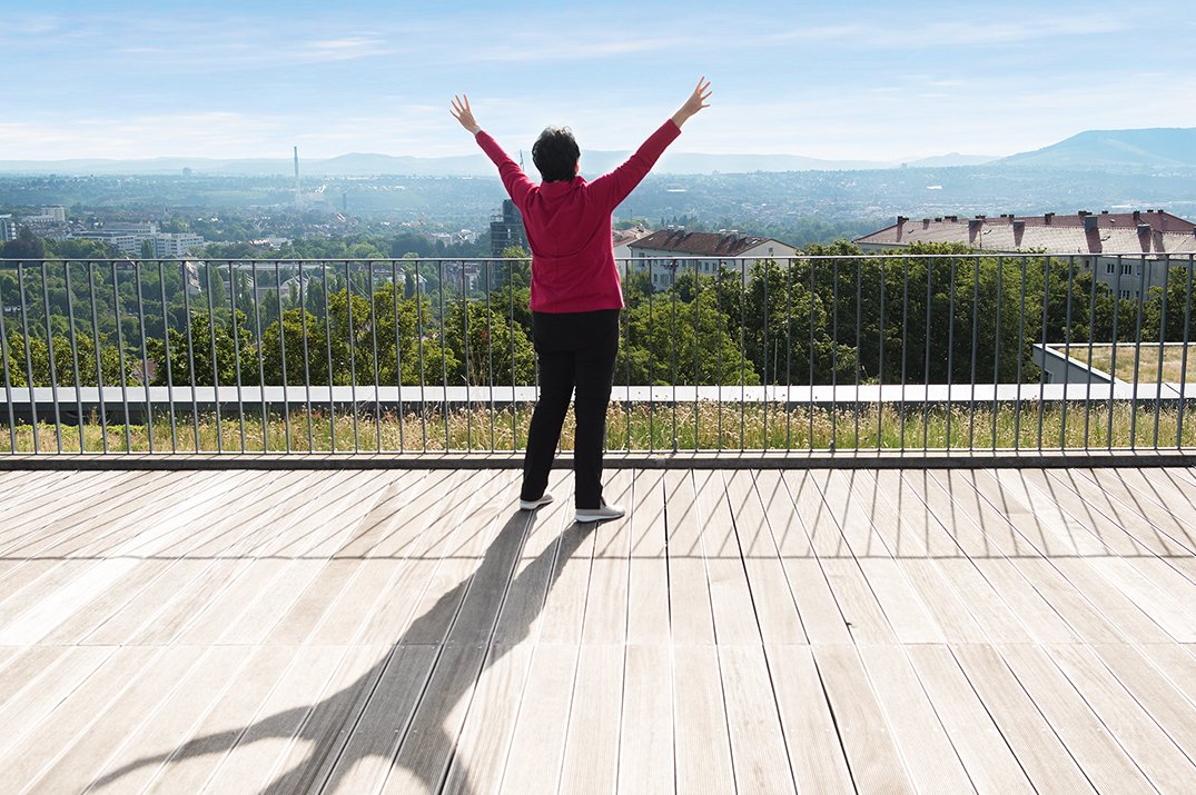 Qi Gong Dame mit ausgebreiteten Armen auf einer Dachterrasse