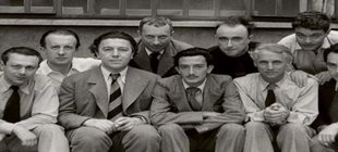 André Breton, Paul Èluard und die Surrealisten André Breton sitz an einem mit Büchern und Papieren beladenen Schreibtisch, mit surrealistischen Werken an der Wand im Hintergrund.