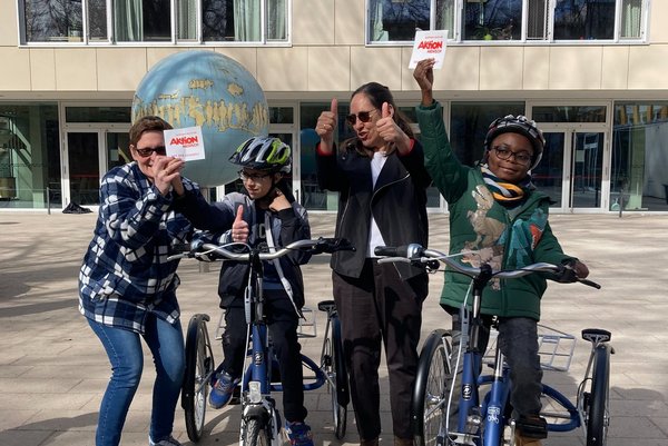 Augustinum Otto-Steiner-Schule Verkehrsunterricht Ein Gruppenbild von zwei Schülern, die jeweils auf einem Dreirad sitzen, und zwei Erwachsenen vor der Otto-Steiner-Schule, die jeweils Daumen nach oben zeigen