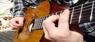 im Ausschnitt des Fotos sind zwei Hände zu sehen, die eine Gitarre halten und spielen