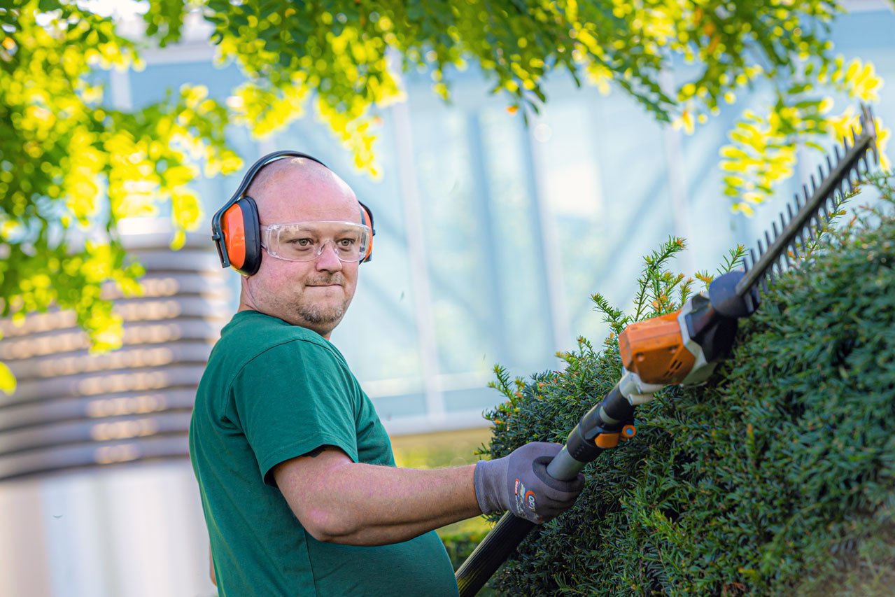 Heckenschneiden Ein Klient der Augustinum Gärtnerei Hollern schneidet mit einer akkubetriebenen Teleskopheckenschere die Hecke