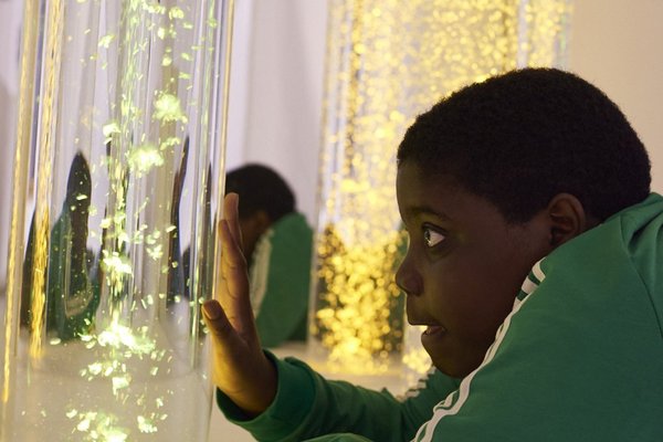 Augustinum Spenden Snoezelenraum Ein Junge liegt in einem Snozelenraum und berührt mit seiner Hand eine Wassersäule