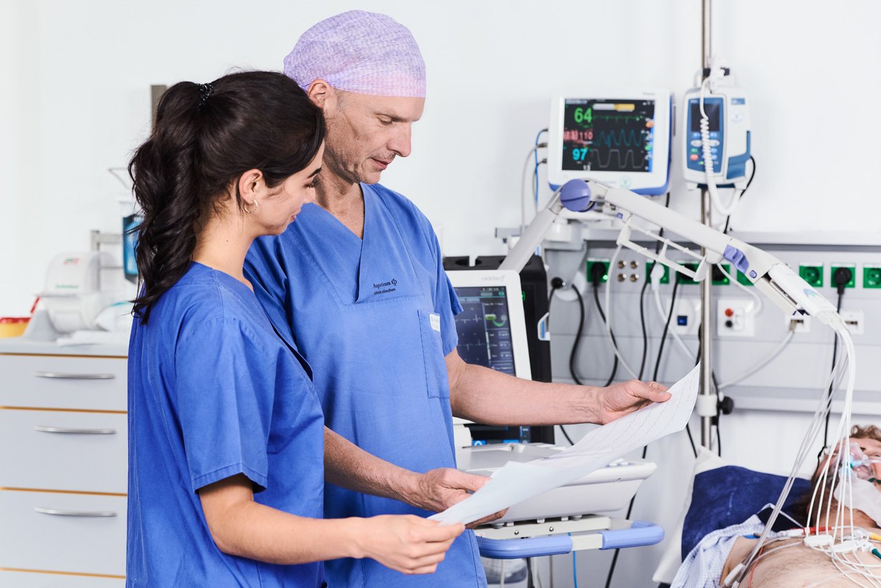Chest Pain Unit - CPU Bild eines Arztes und einer Pflegerin bei der Kontrolle des EKGs eines Patienten mit einem Link zur Chest Pain Unit der Augustinum Klinik