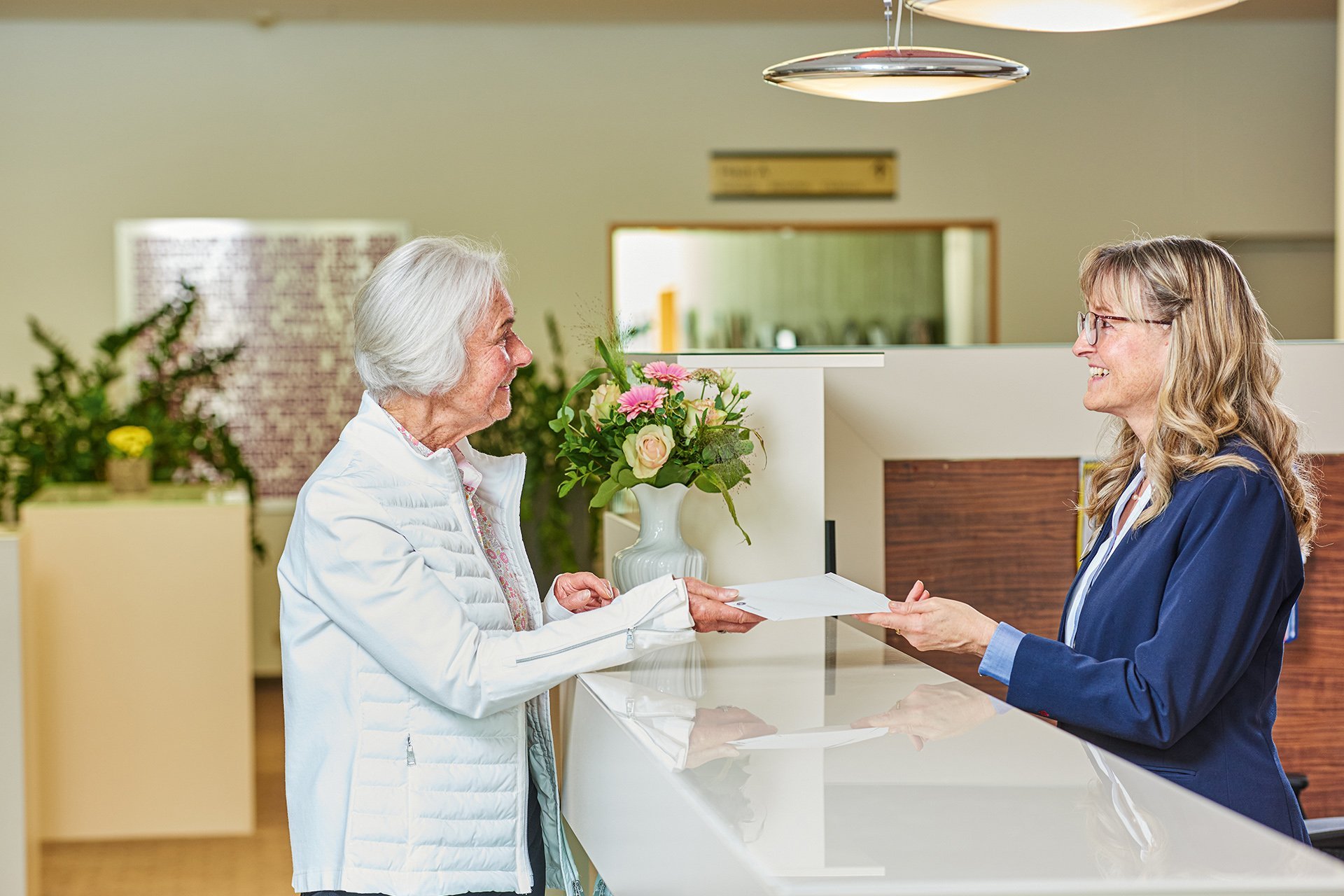 Augustinum Seniorenresidenz Kassel Empfang Eine Mitarbeiterin des Empfangs übergibt einen Brief an eine Seniorin