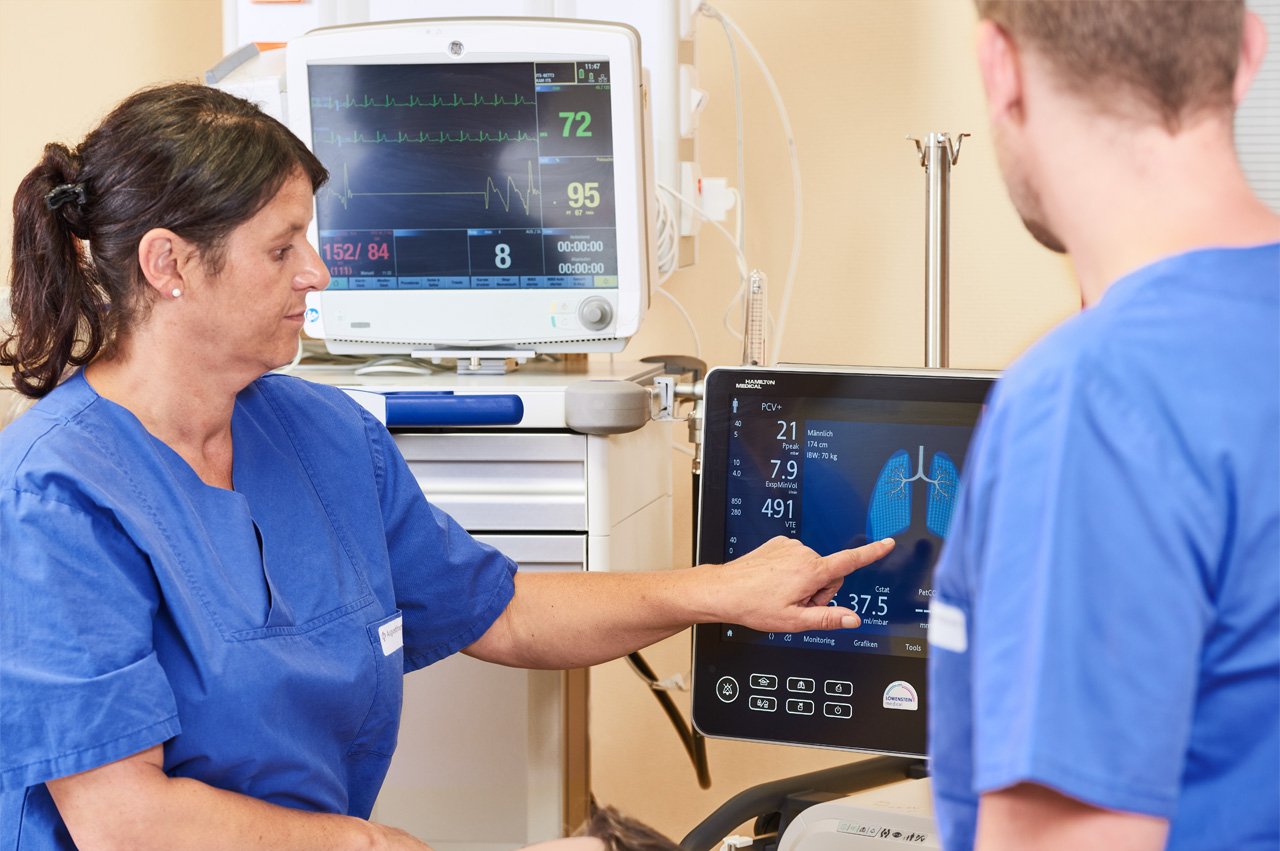 Intensivstation Eine Pflegerin und ein Arzt stehen vor Bildschirmen, die medizinische Daten anzeigen