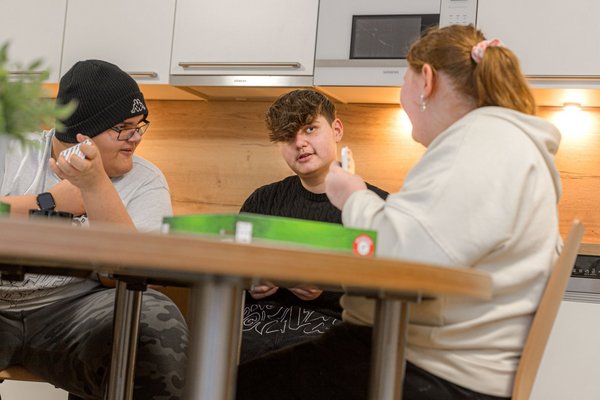 Augustinum Fördermagazin Adipositas Wohngruppe Drei Jugendliche der Adipositas Wohngruppen sitzen an einem Tisch und spielen ein Kartenspiel