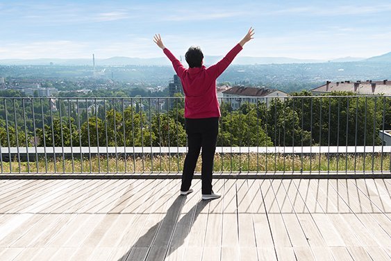 Qi Gong Eine Seniorin steht mit nach oben gestreckten Armen auf einer Terrasse