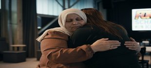 Trauernde Frau mit Kopftuch umarmt eine andere Frau