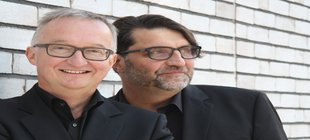 Notizen aus der kirchlichen Provinz Die beiden Kabarettisten Peter Schaal-Ahlers und Søren Schwesig stehen vor einer gemauerten, weißen Wand.