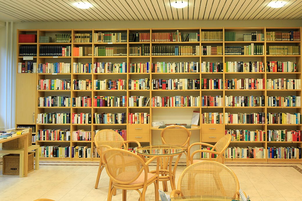 In der Bibliothek finden die Bewohner reichlich „Lesefutter“. Bibliothek mit Stühlen und Bücherregal