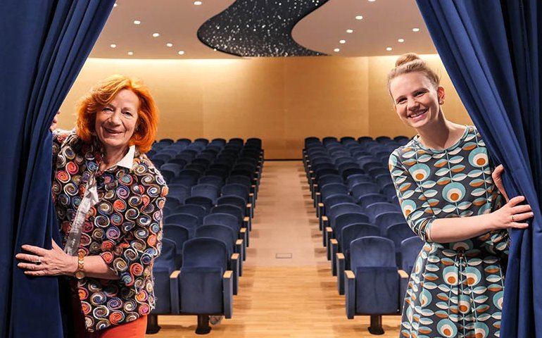 Zwei Kulturreferentinnen ziehen den Bühnenvorhang zur Seite; Theatersaal im Hintergrund