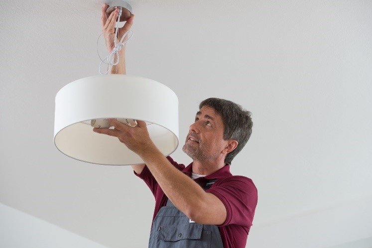 Kleinreparaturen werden von hauseigenen Handwerkern erledigt Handwerker beim Befestigen einer Deckenlampe