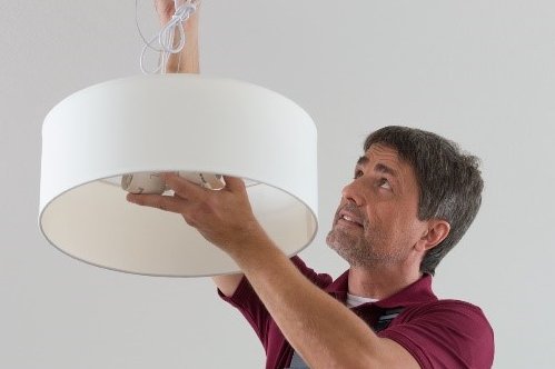 Kleinreparaturen werden von hauseigenen Handwerkern erledigt Handwerker beim Befestigen einer Deckenlampe