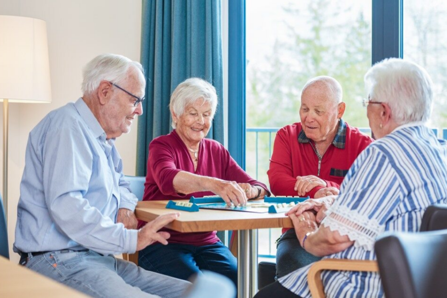 Augustinum Berchtesgadener Land Seniorenwohnen Gesellschaftsspiel Vier Senior*inne sitzen gemeinsam an einem Tisch und spielen ein Gesellschaftsspiel