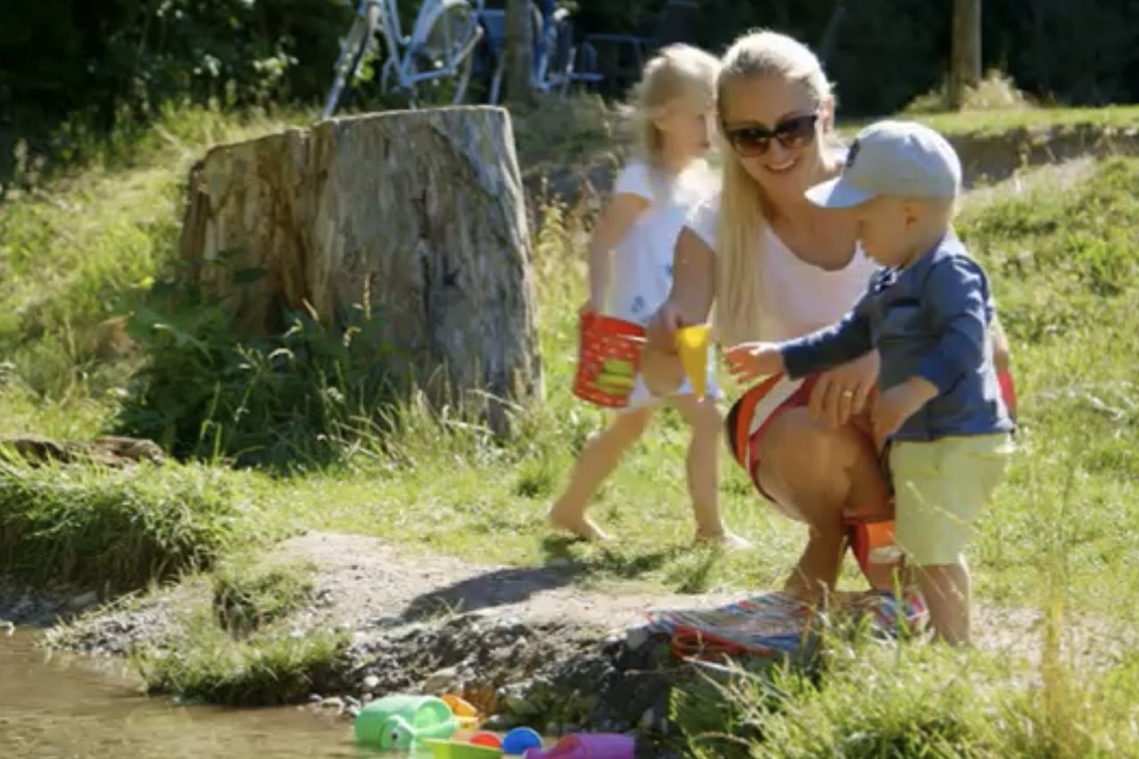 Job und Familie vereint Eine Mutter spielt an einem Teich mit ihrem Sohn und ihrer Tochter