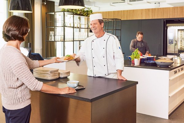 Der Service im Vierundsiebzig Ein Koch des Vierundsiebzig überreicht einer Kundin ihr Gericht aus der offenen Showküche