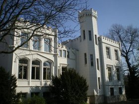 Ein weißes Gebäude mit Zinnen und Turm vor einem blauen Himmel