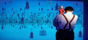 Humor ist, wenn man trotzdem lacht Schauspieler Nobert Eilts steht im heißen Hemd und Hosenträgern vor einer Leinwand mit dem Rücken zum Publikum, über seine Schulter lugt eine Kasperle-Puppe.