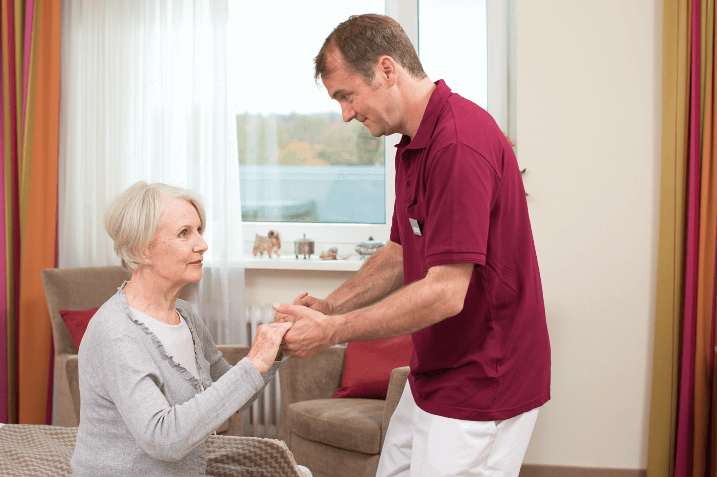 Tagesbetreuung für Menschen mit Demenz Pfleger hilft älterer Dame beim Aufstehen