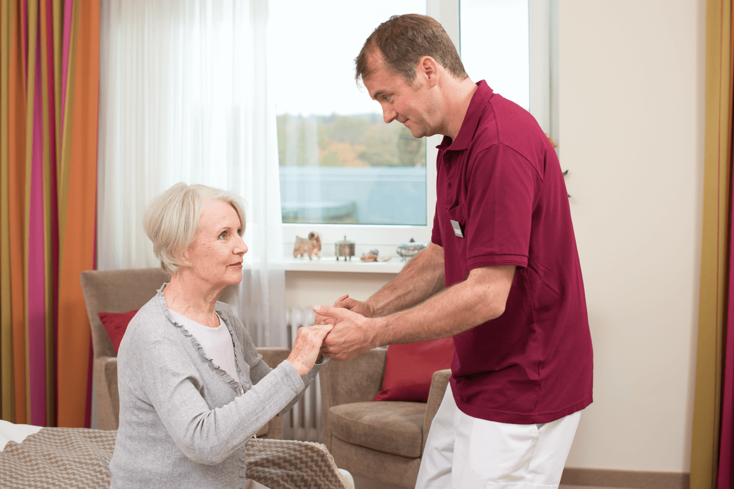 Tagesbetreuung für Menschen mit Demenz Pfleger hilft älterer Dame beim Aufstehen