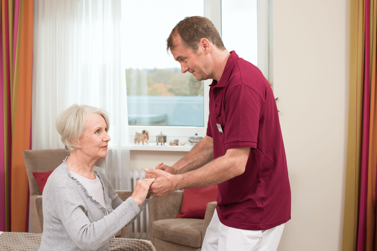 Tagesbetreuung für Menschen mit Demenz Pfleger hilft älterer Dame beim Aufstehen