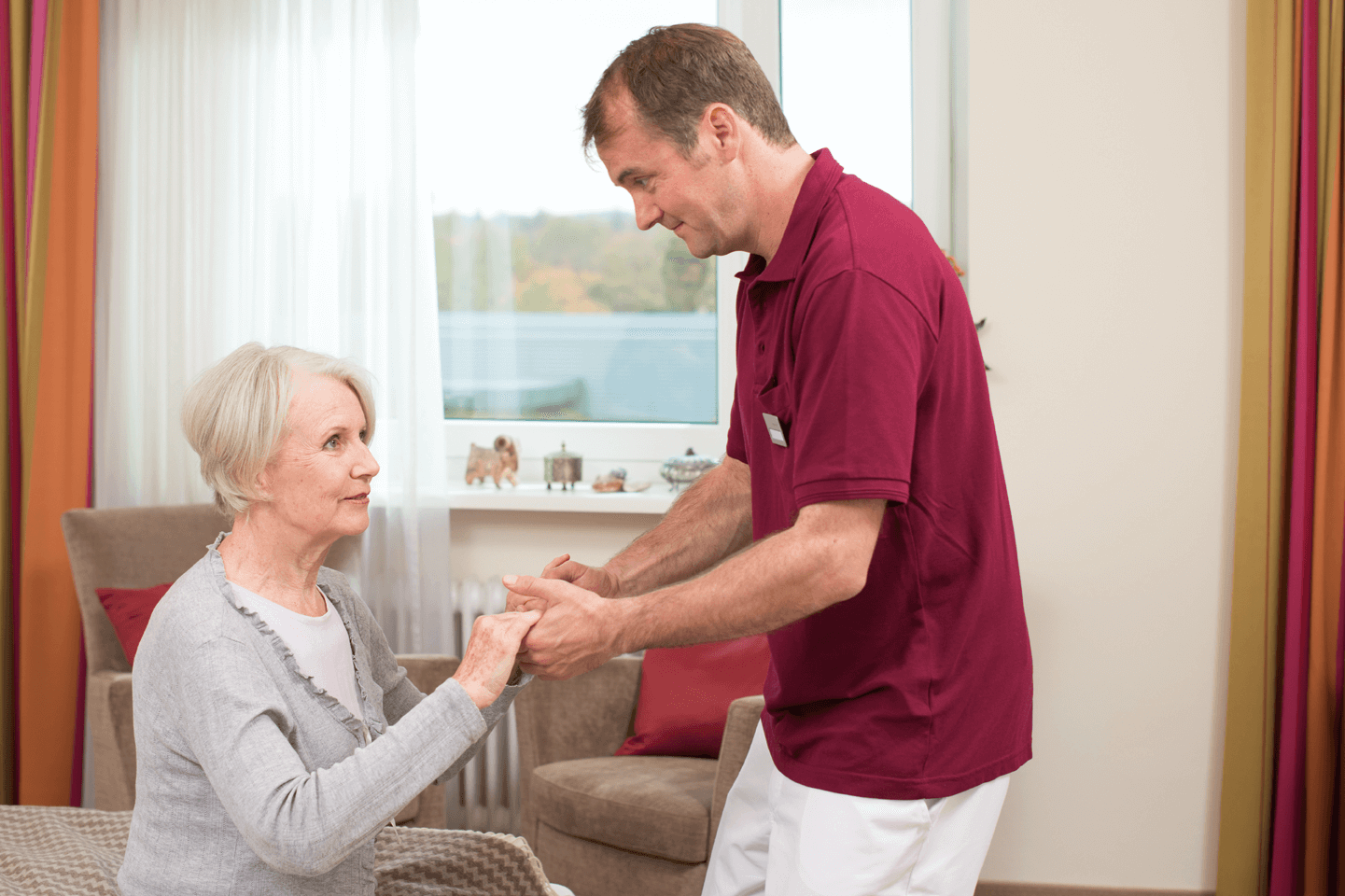 Tagesbetreuung für Menschen mit Demenz Pfleger hilft älterer Dame beim Aufstehen