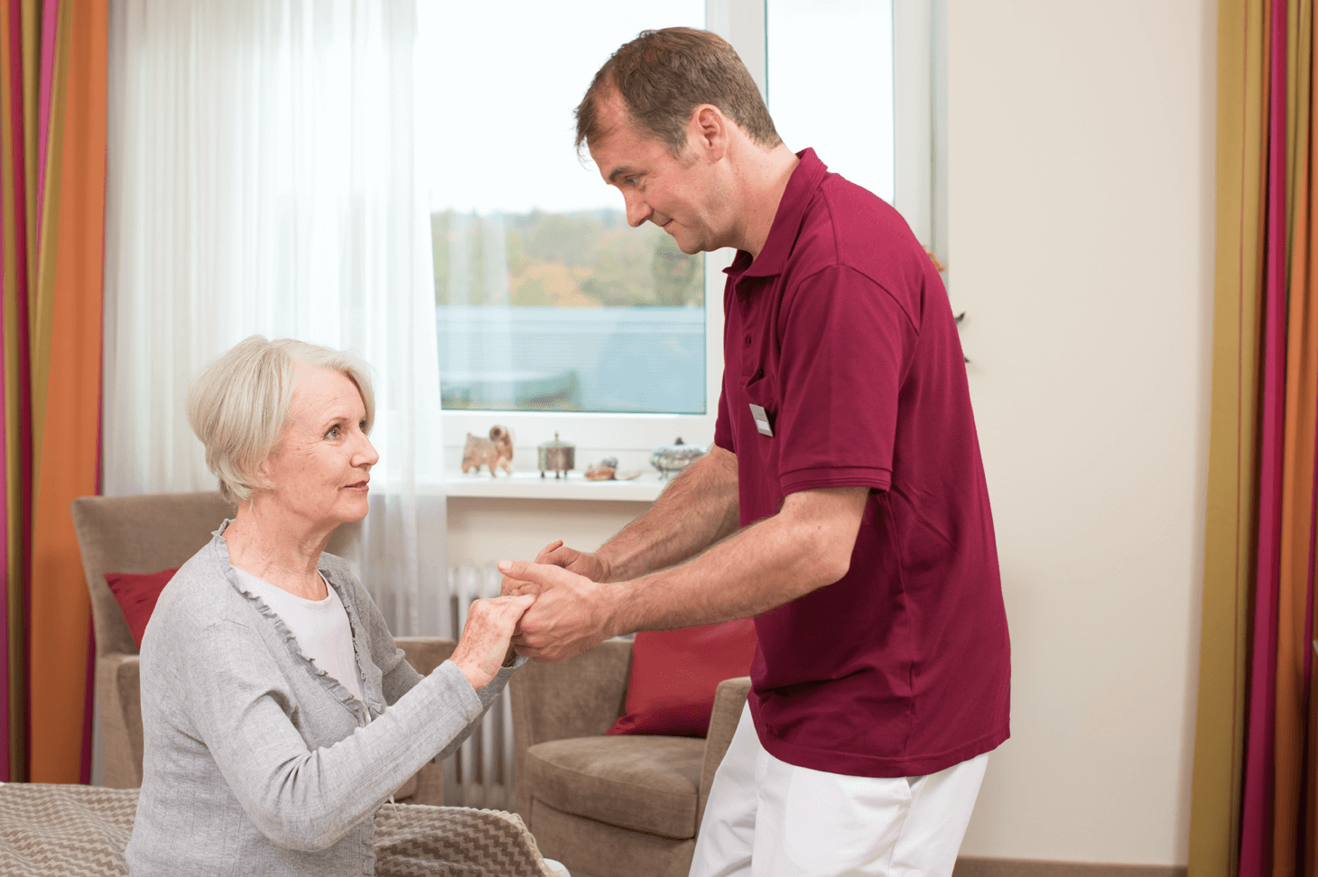 Tagesbetreuung für Menschen mit Demenz Pfleger hilft älterer Dame beim Aufstehen
