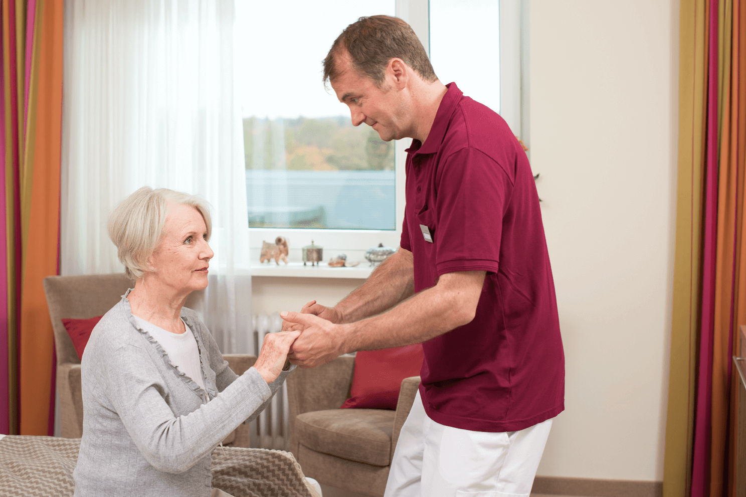 Tagesbetreuung für Menschen mit Demenz Pfleger hilft älterer Dame beim Aufstehen